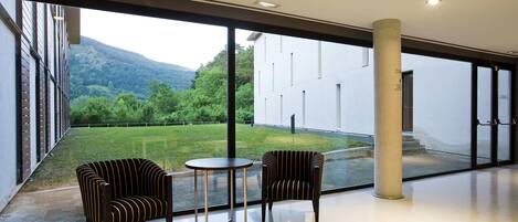 Un interior moderno con ventanas amplias, dos sillones a rayas, una mesa redonda pequeña y vistas a un paisaje verde.