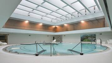 A large indoor swimming pool with a glass ceiling, multiple lanes, and a central diving area.