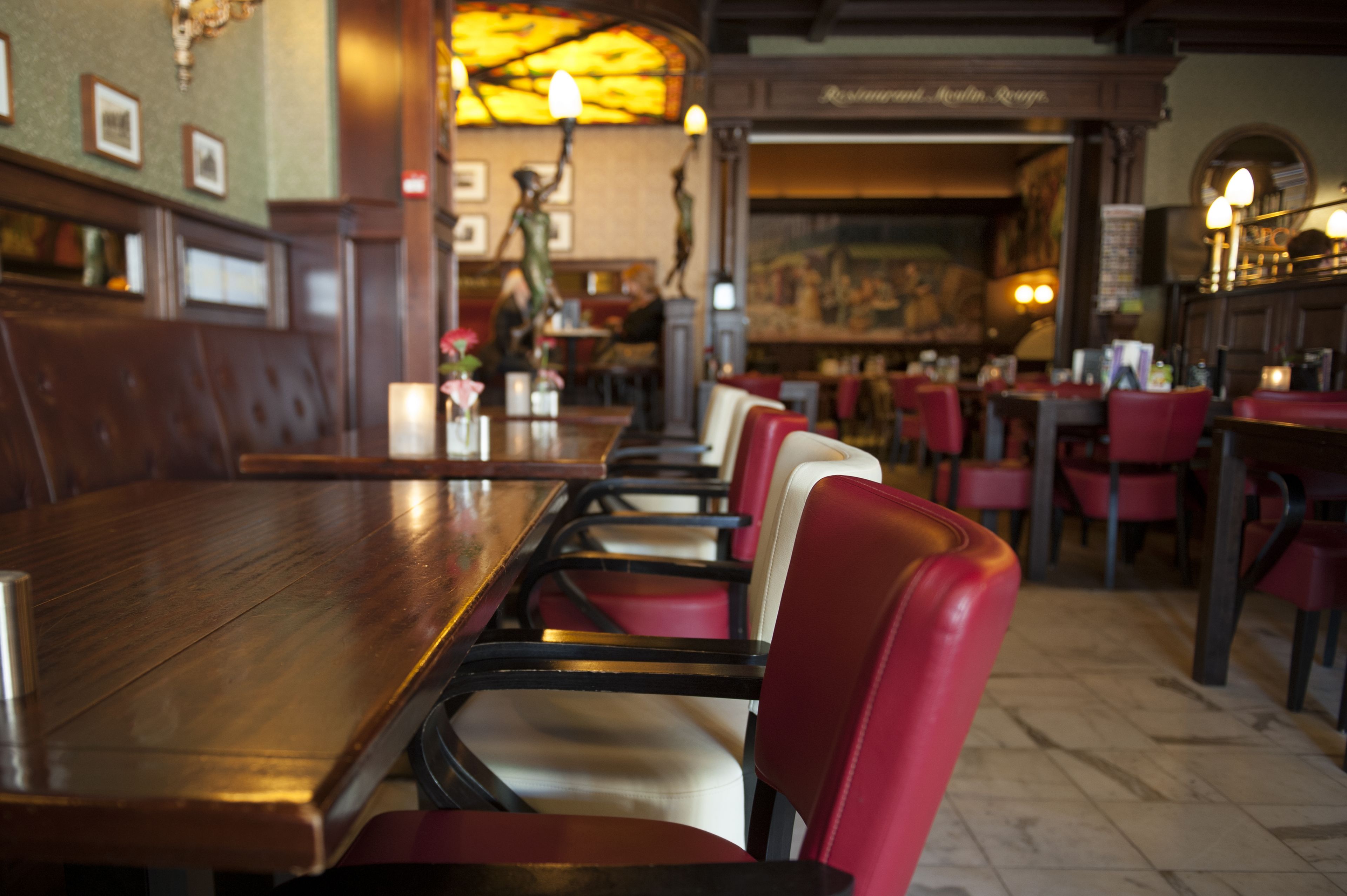 Interior de restaurante con mesas de madera y sillas tapizadas en rojo.