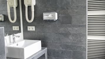 Un baño moderno con un lavamanos blanco, paredes revestidas de baldosas oscuras y un perchero.