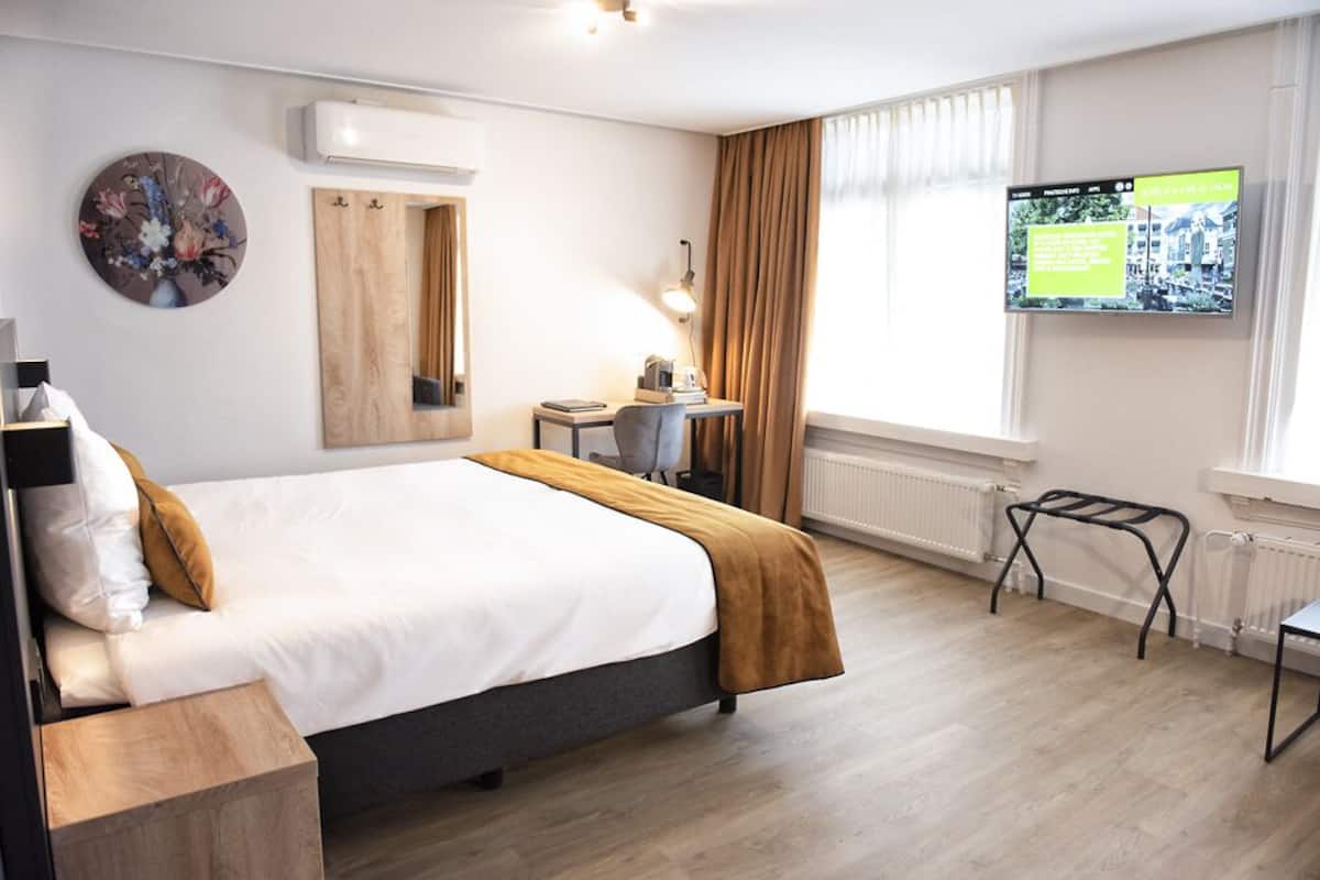 A hotel room with a bed, a desk, a chair, a TV, and a window with curtains.