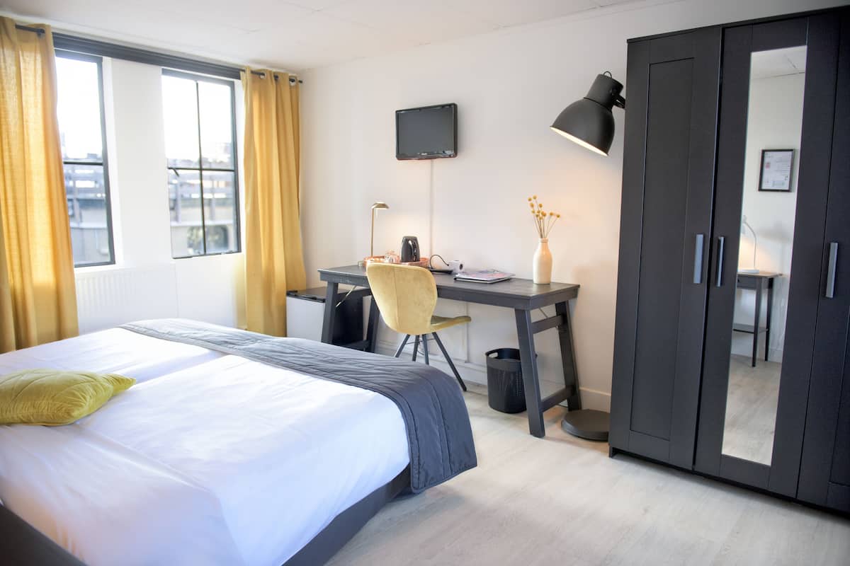 A hotel room with a bed, desk, chair, and wardrobe.