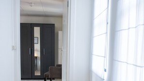 Un pasillo con piso de madera, una puerta oscura y una ventana con persianas.