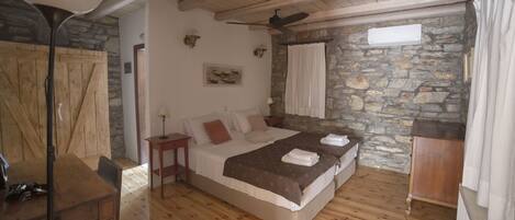 Un dormitorio con piso de madera, cama con manta marrón, ventilador de techo y pared de piedra.