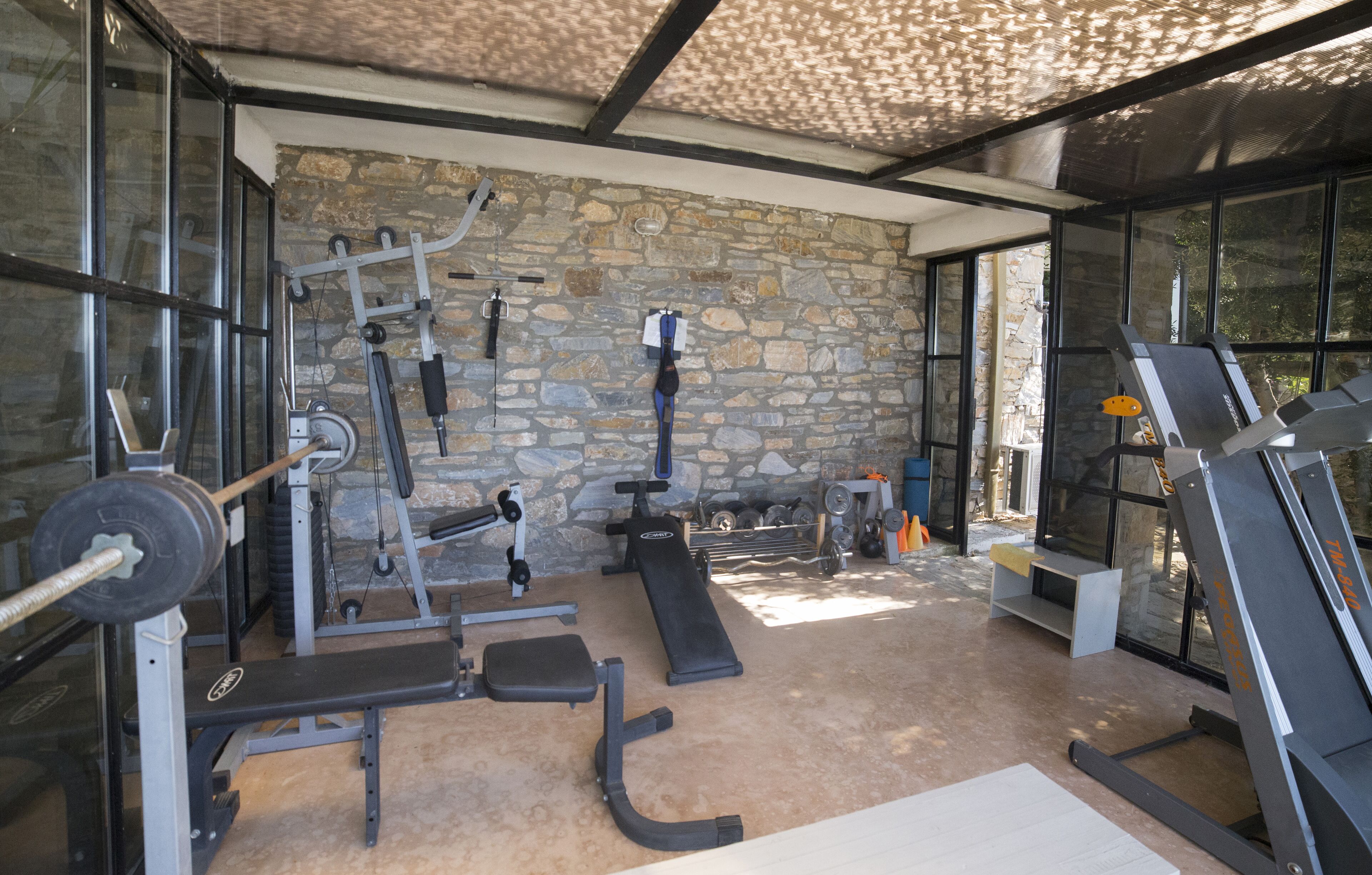 Una palestra con diverse attrezzature per esercizi, pareti in pietra e ampie finestre.