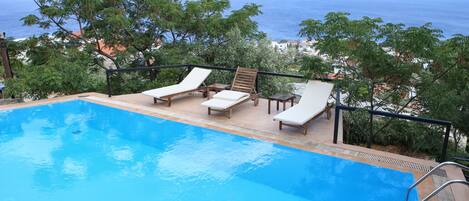 A pool with lounge chairs and a view of the ocean.