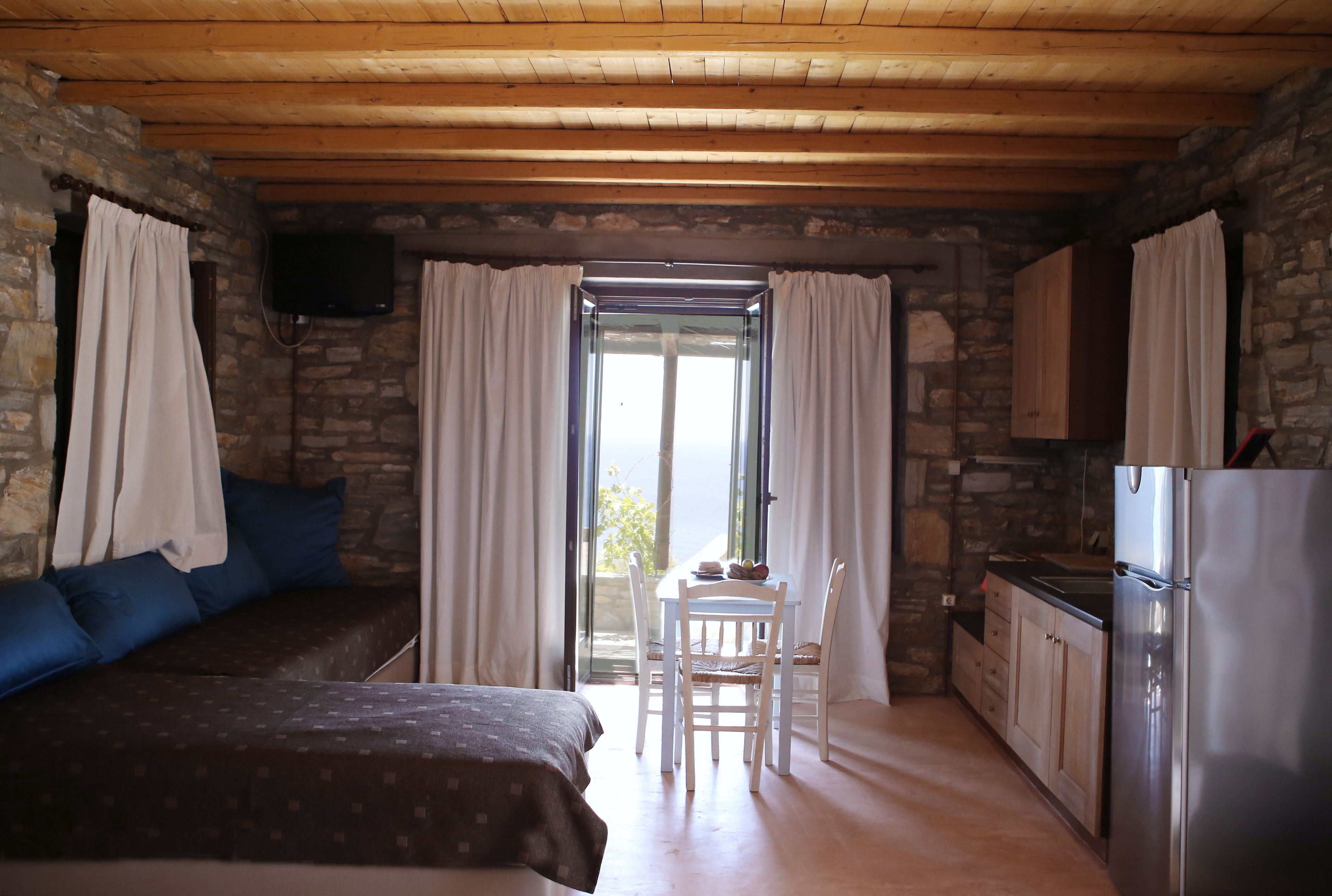 A cozy room with a bed, a dining table with chairs, a kitchen area, and a stone wall.
