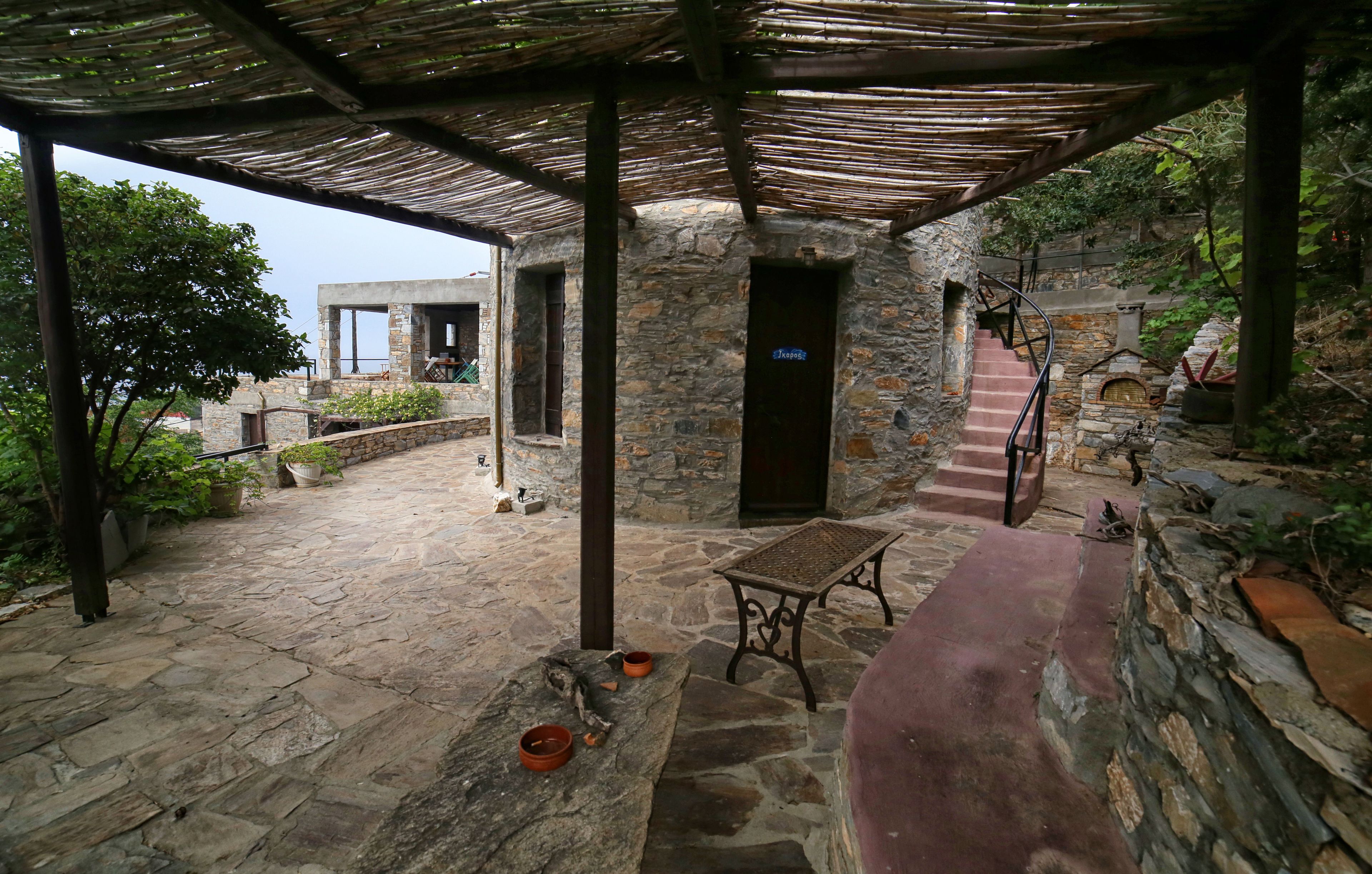A stone-paved courtyard with a wooden pergola, stone walls, and a staircase leading to an upper level.