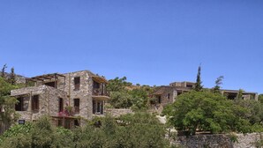 A stone building with multiple windows and balconies, surrounded by trees and a clear blue sky. - Pyrgos Ikaria Traditional Village (Ikaria)