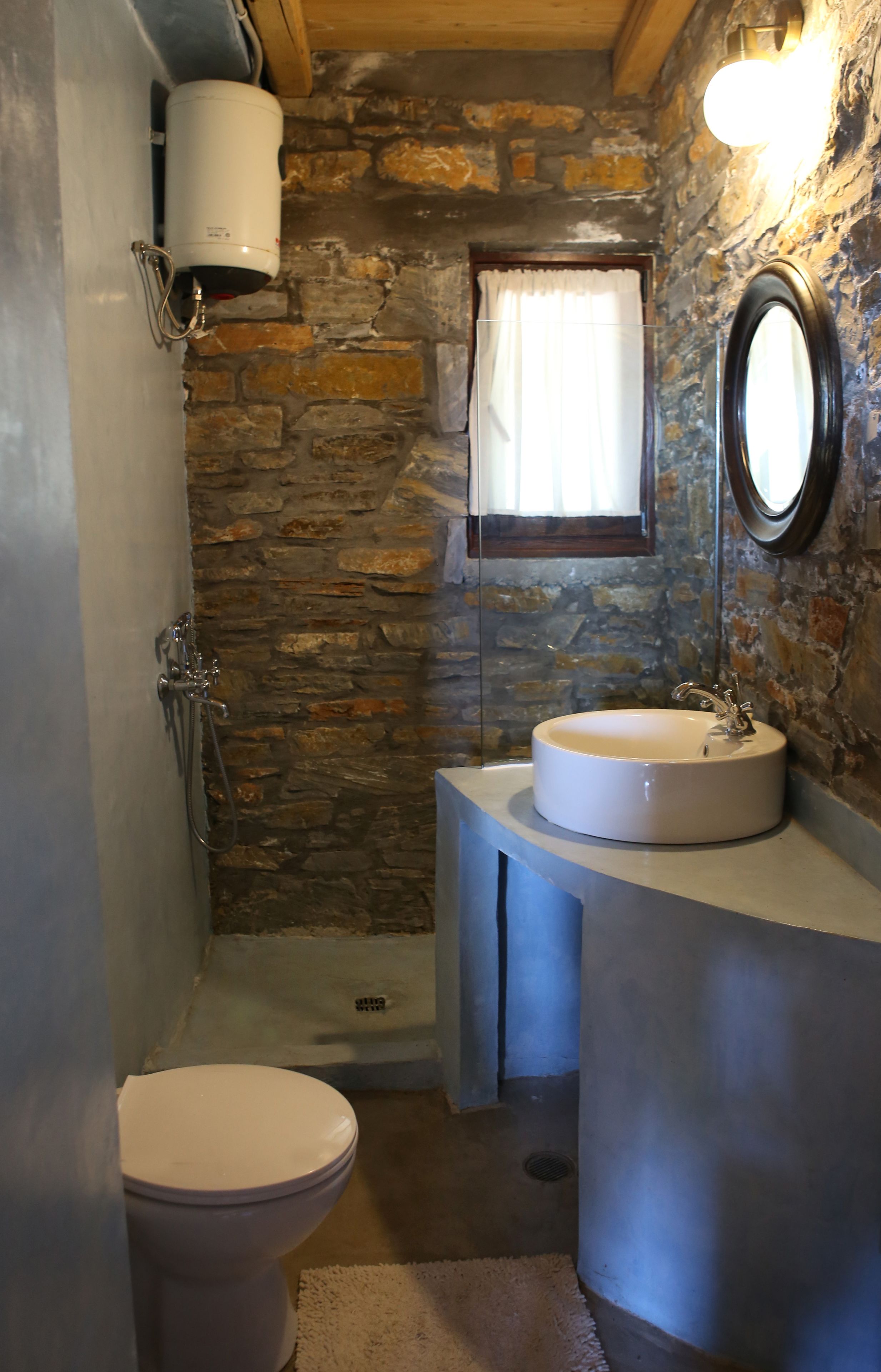A bathroom with a stone wall, a white sink, a toilet, and a shower.