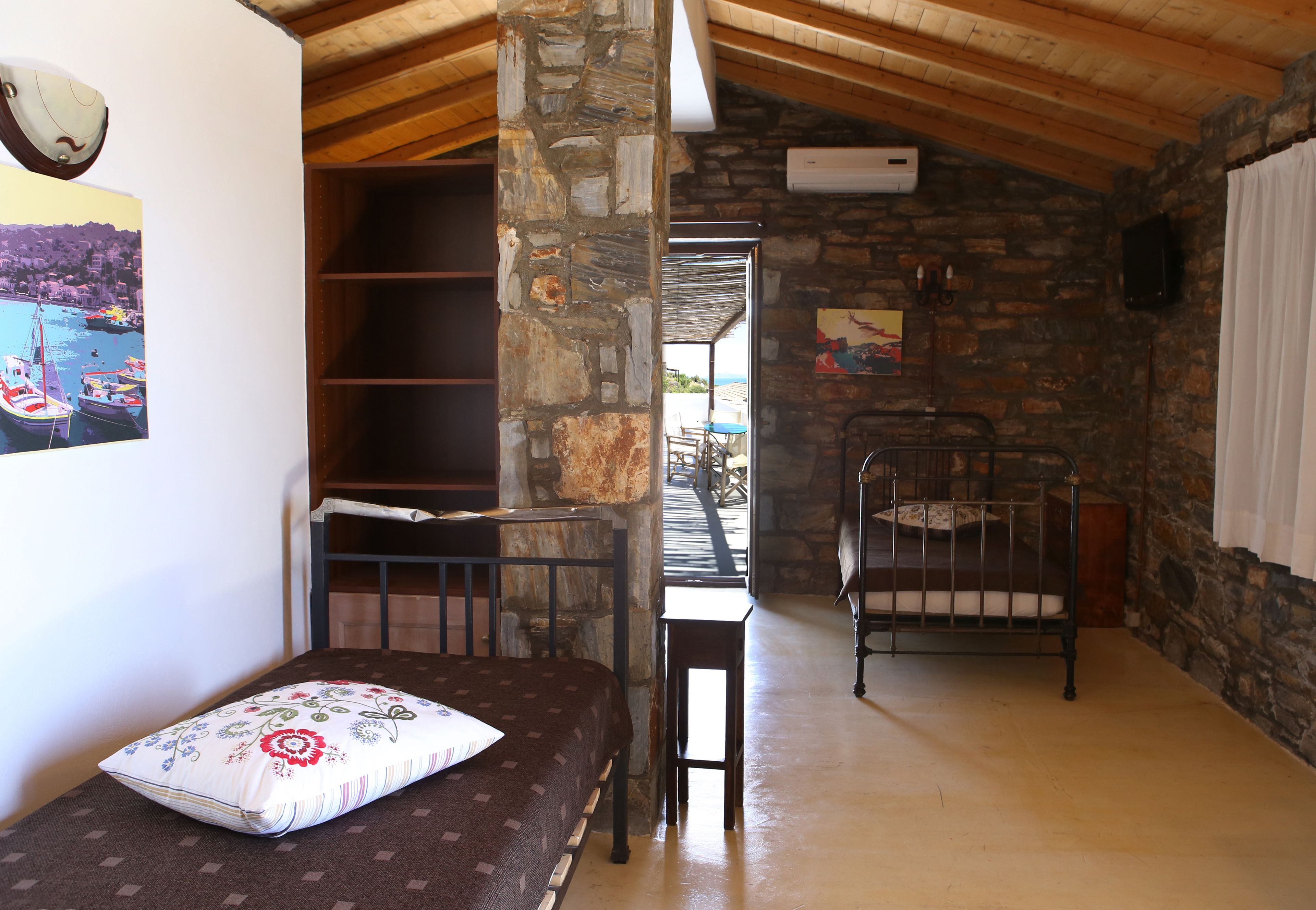 Una habitación acogedora con pared de piedra, techo de madera, cama con cojín floral, una mesita y una silla de metal.