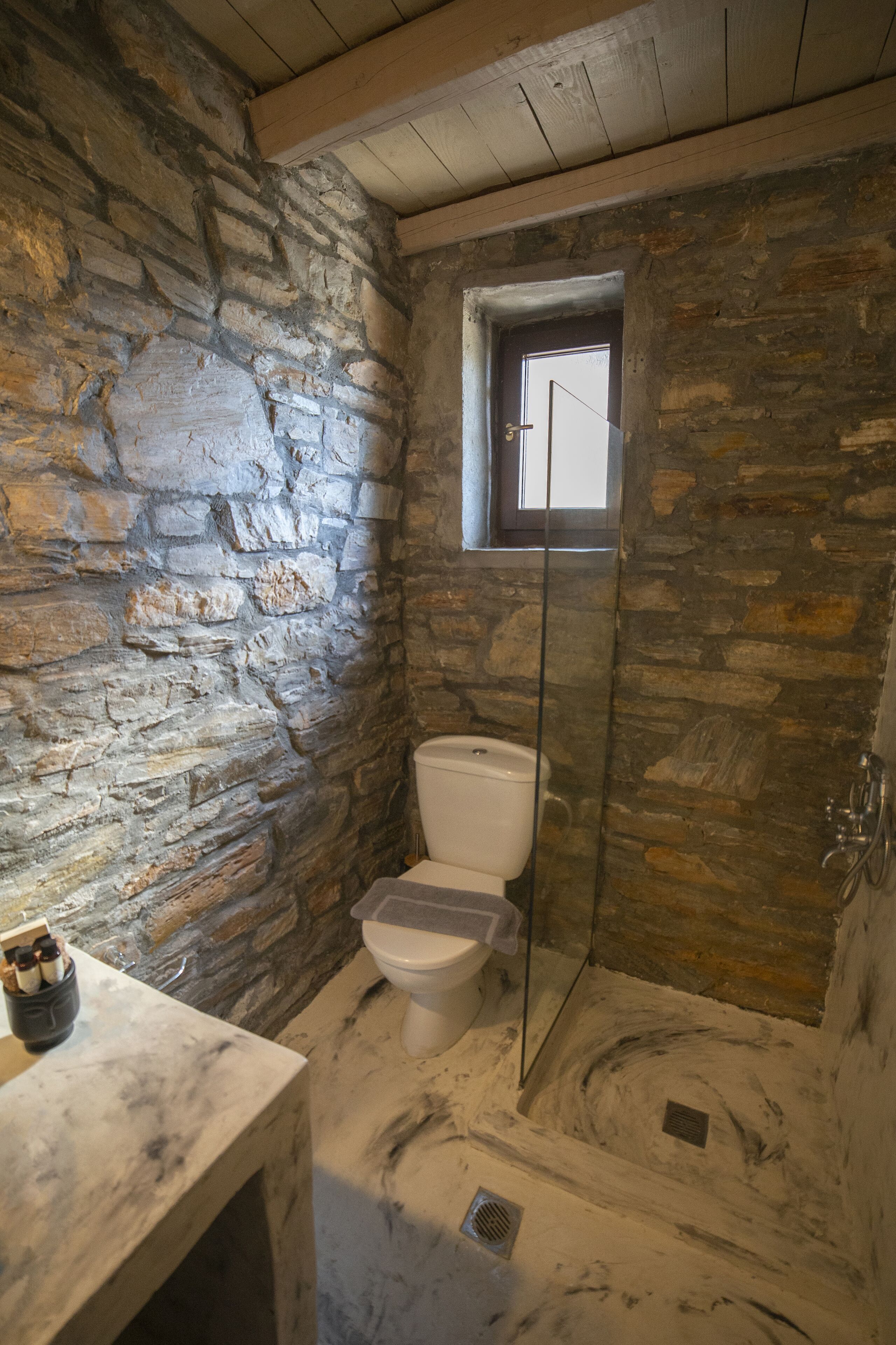 A stone-walled bathroom with a toilet, a shower, and a small window.