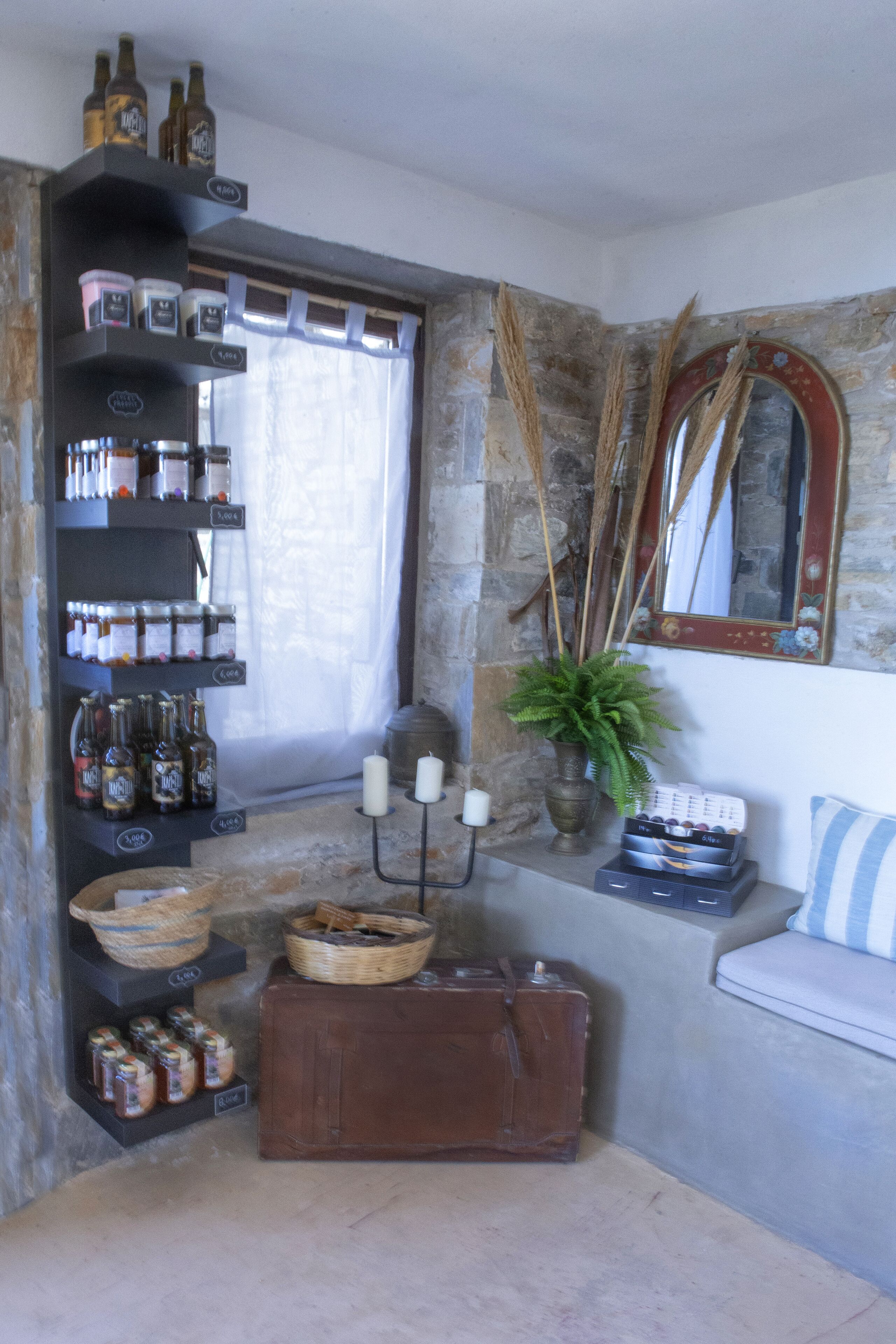 A cozy corner with a stone wall, a shelf with bottles, a potted plant, candles, and a vintage suitcase.