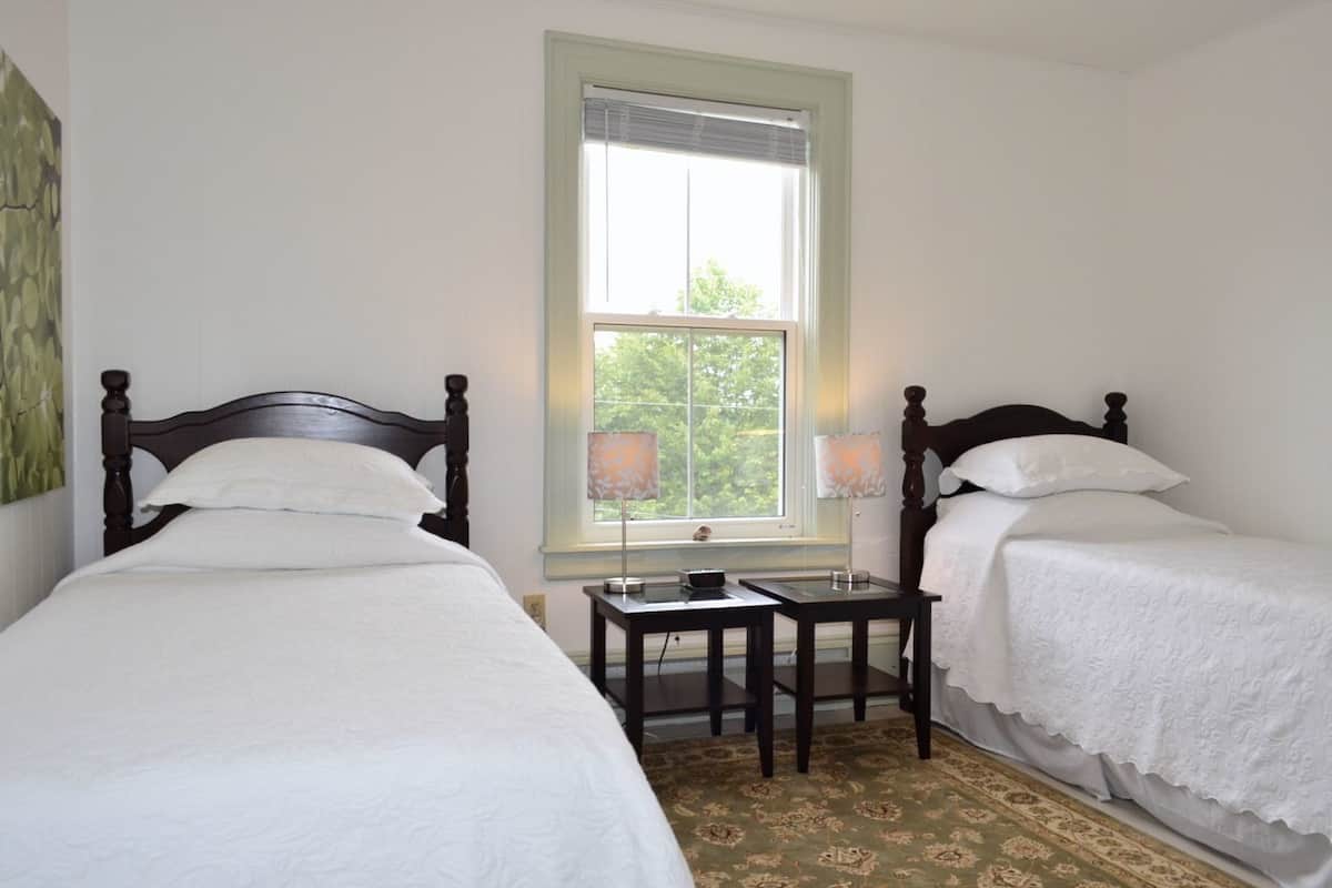 A room with two single beds, a small table, and a window with blinds.