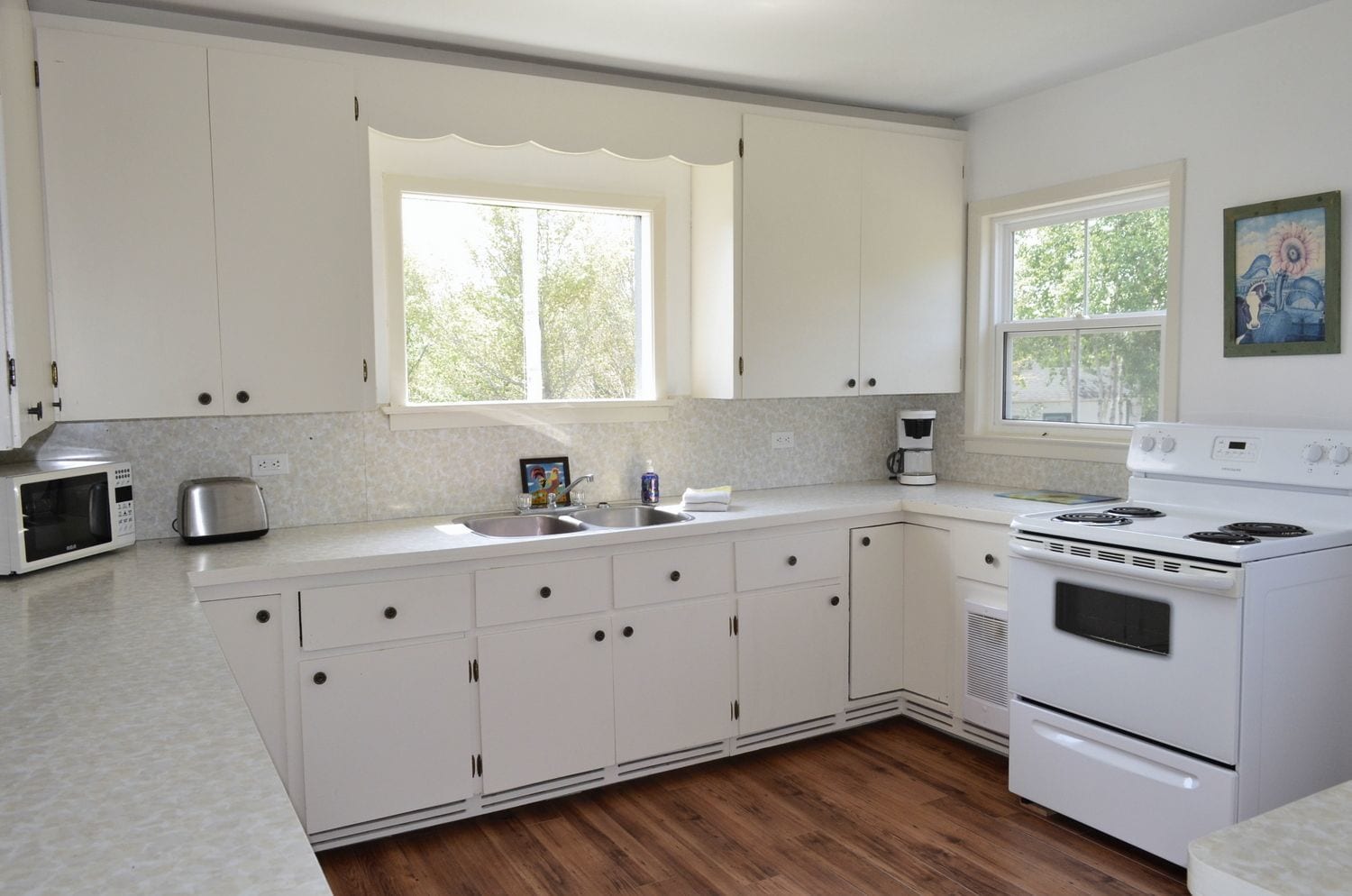 A kitchen with white cabinets, a double sink, a toaster, a coffee maker, and a stove.