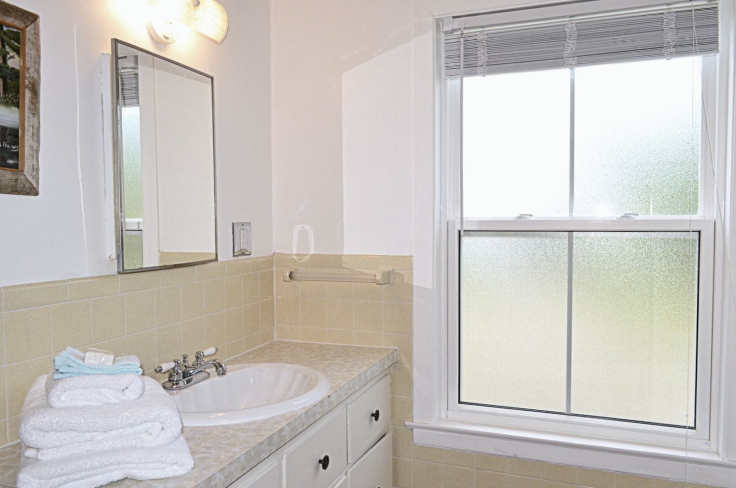 A bathroom with a sink, mirror, towel rack, and a frosted window.