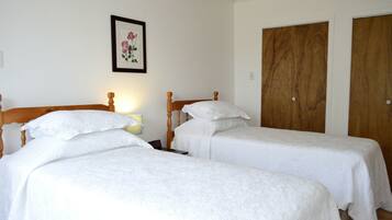 A room with two single beds, wooden headboards, white bedding, a framed floral artwork on the wall, and wooden doors.