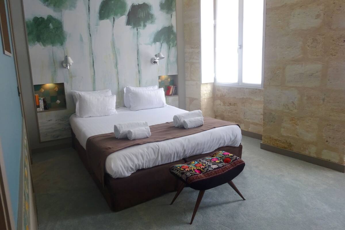 A bedroom with a large bed, a bench, and a wall with a tree painting.
