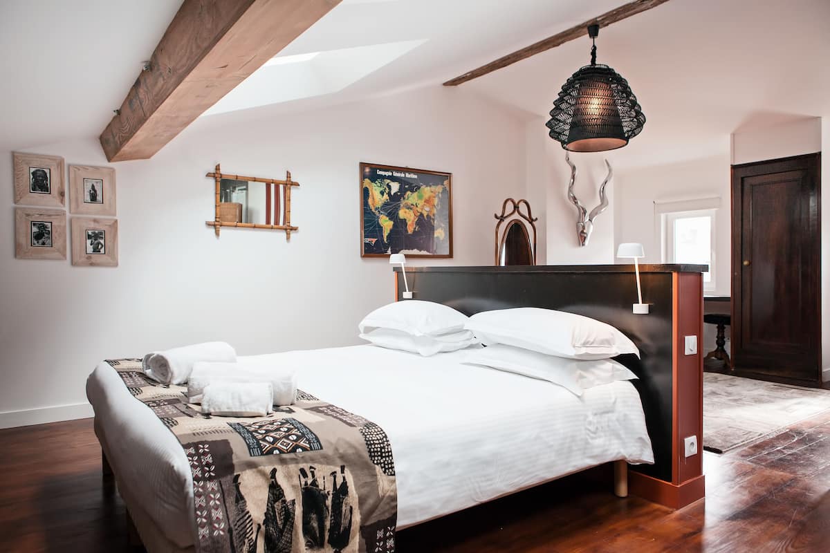 A neatly made bed with white linens and a patterned throw blanket, a wooden headboard, and a hanging lamp.