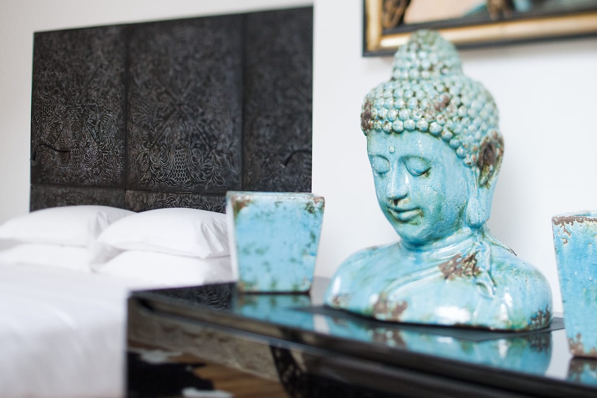 A bedroom with a bed, a headboard, and a Buddha statue on a table.