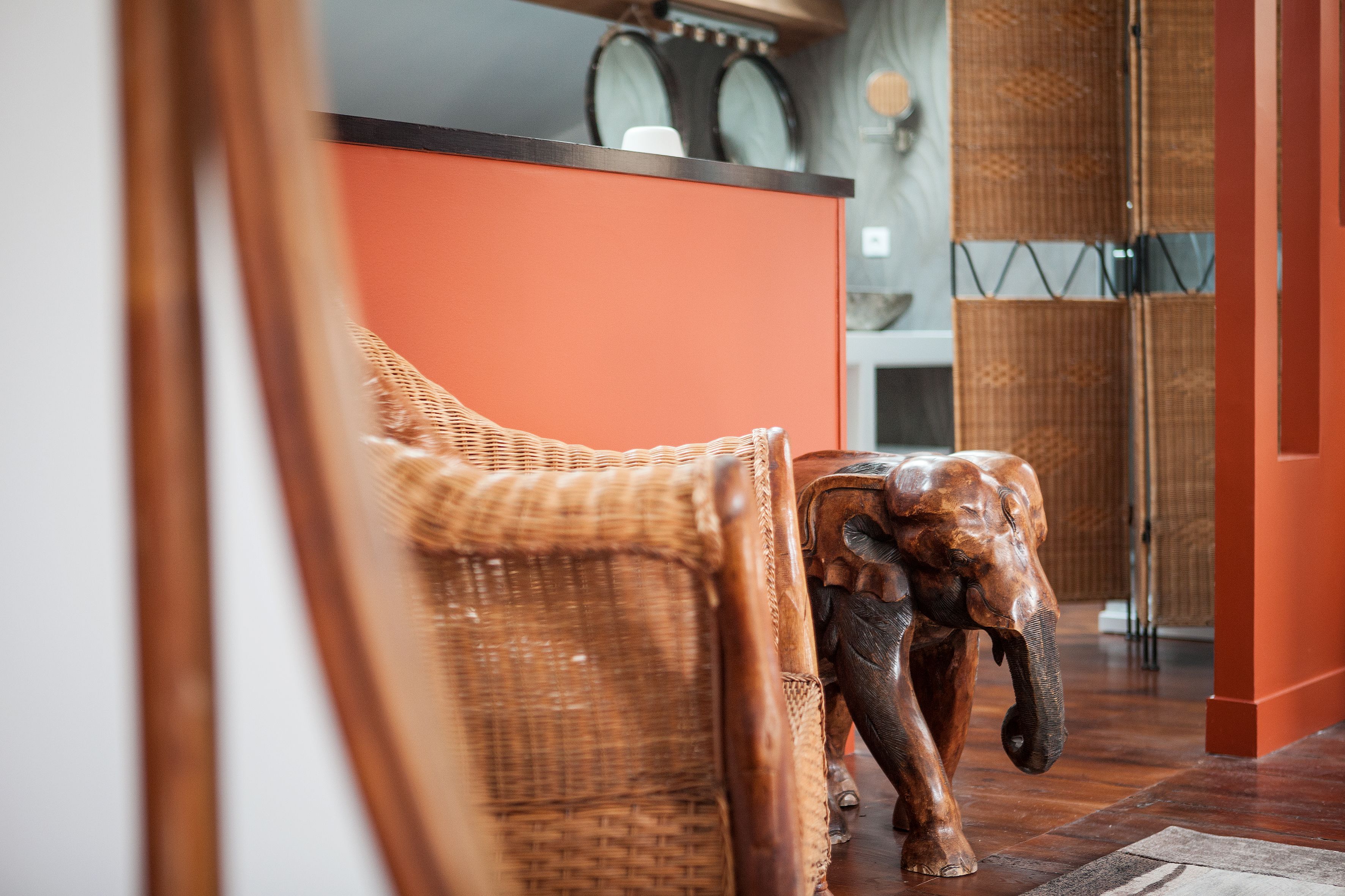 A wicker chair and a wooden elephant sculpture in a room with an orange wall and a wooden floor.