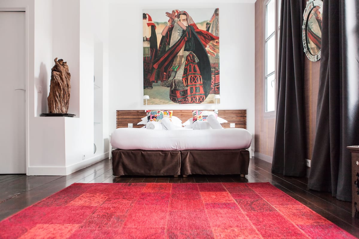 A modern hotel room with a large bed, a red carpet, a wooden headboard, and a painting on the wall.