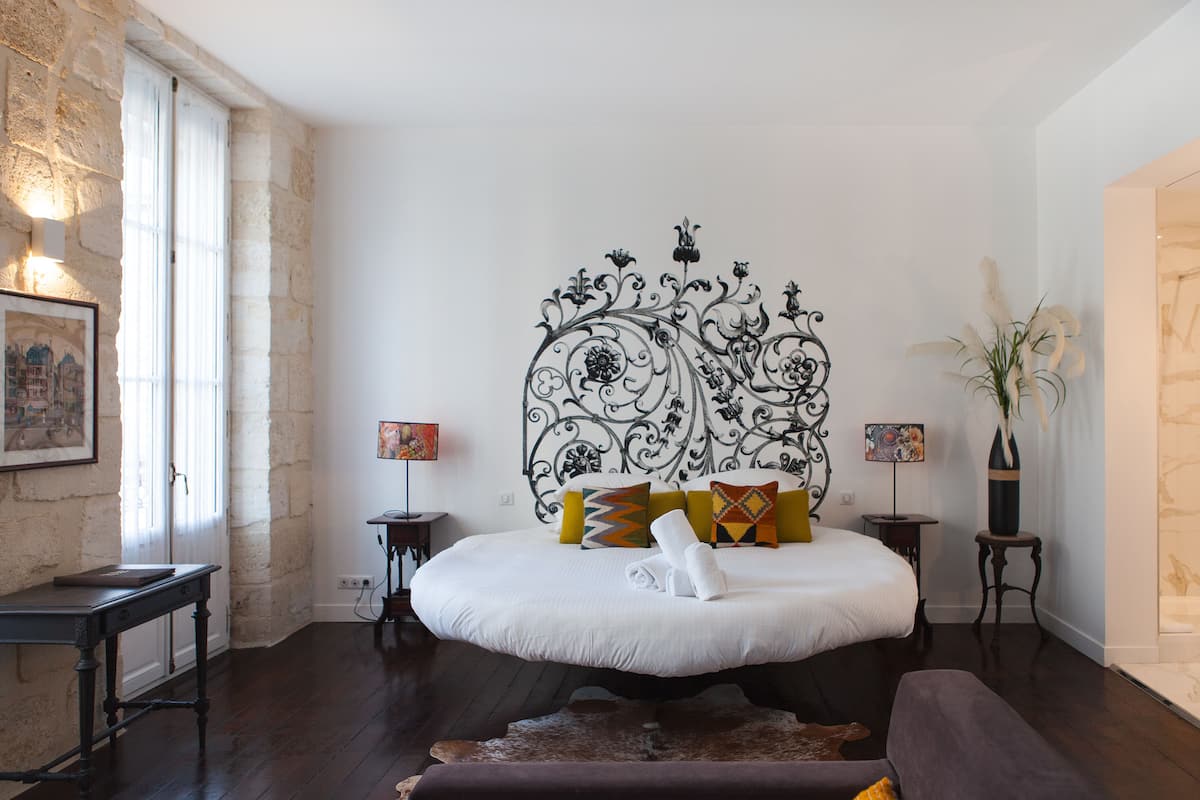 A bedroom with a large bed, a decorative headboard, a stone wall, and a wooden floor.