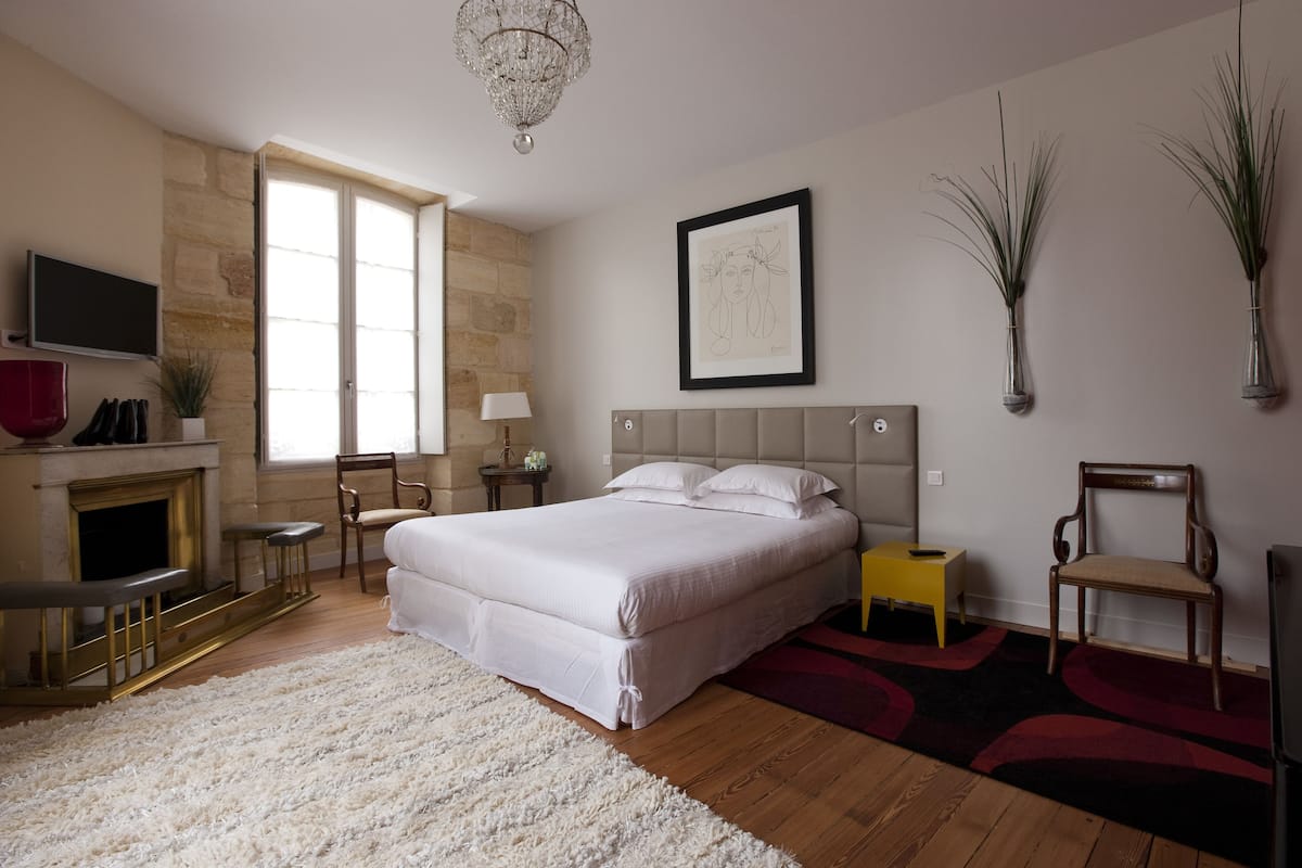 A bedroom with a large bed, a fireplace, a TV, and a chandelier.