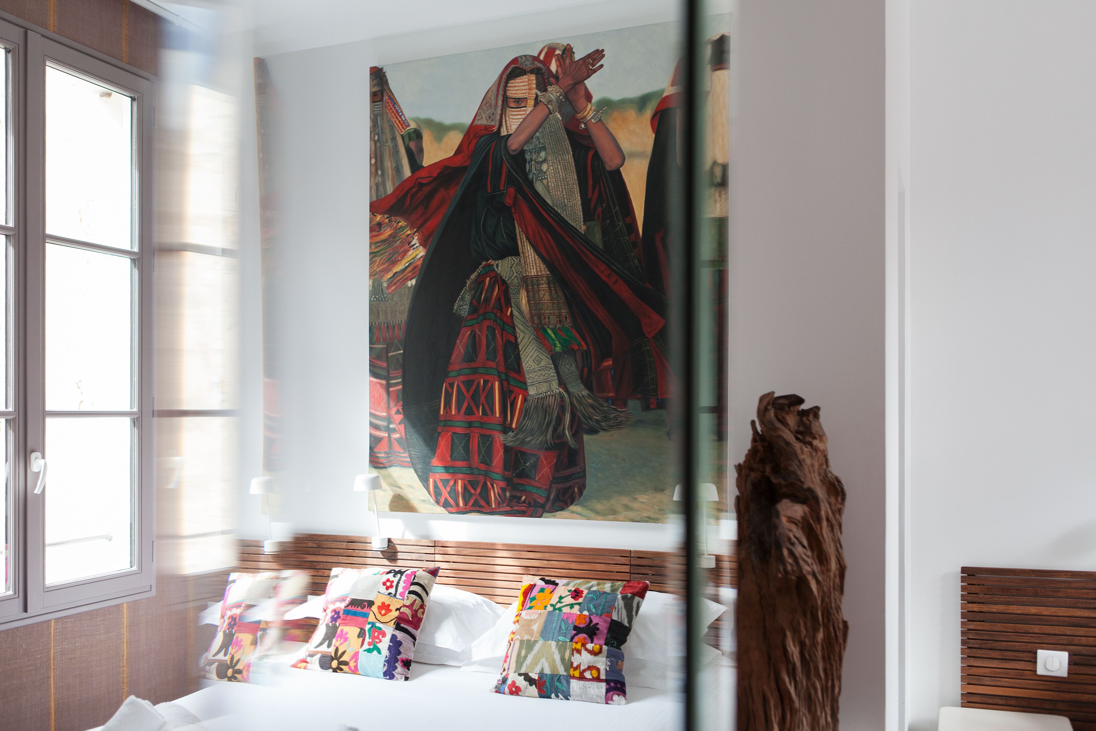 Ein Hotelzimmer mit einem großen Gemälde einer traditionellen Figur, einem hölzernen Kopfbrett und einer dekorativen Holzskulptur.