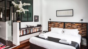 A modern bedroom with a large bed, a bookshelf, and a decorative plant. - Une Chambre chez Dupont (Bordeaux)
