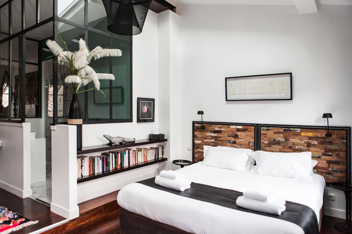 A modern bedroom with a large bed, a bookshelf, and a decorative plant.