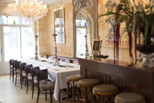 A restaurant with a long table set for dining, wooden chairs, and a bar area with stools.