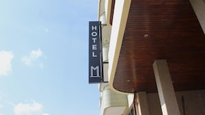 Un letrero de hotel con diseño moderno, colocado en un edificio de fachada de madera y un cielo azul despejado al fondo.