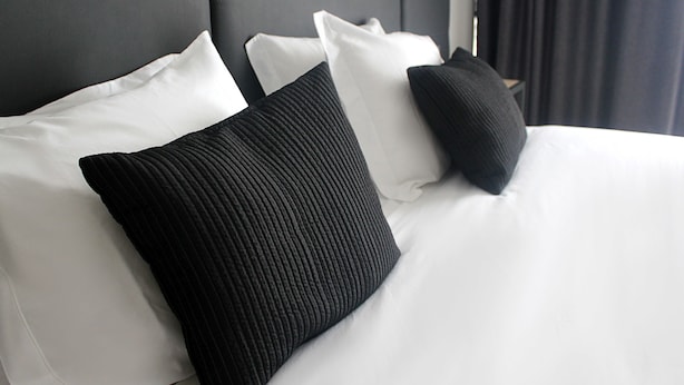 Una cama bien tendida con almohadas blancas y negras, cabecera oscura y diseño de habitación moderno.