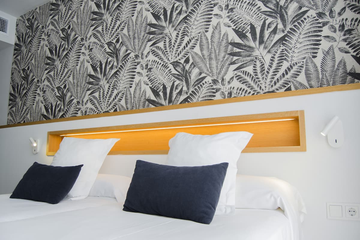 A hotel room with a bed, two pillows, a headboard, and a wall with a leaf pattern.