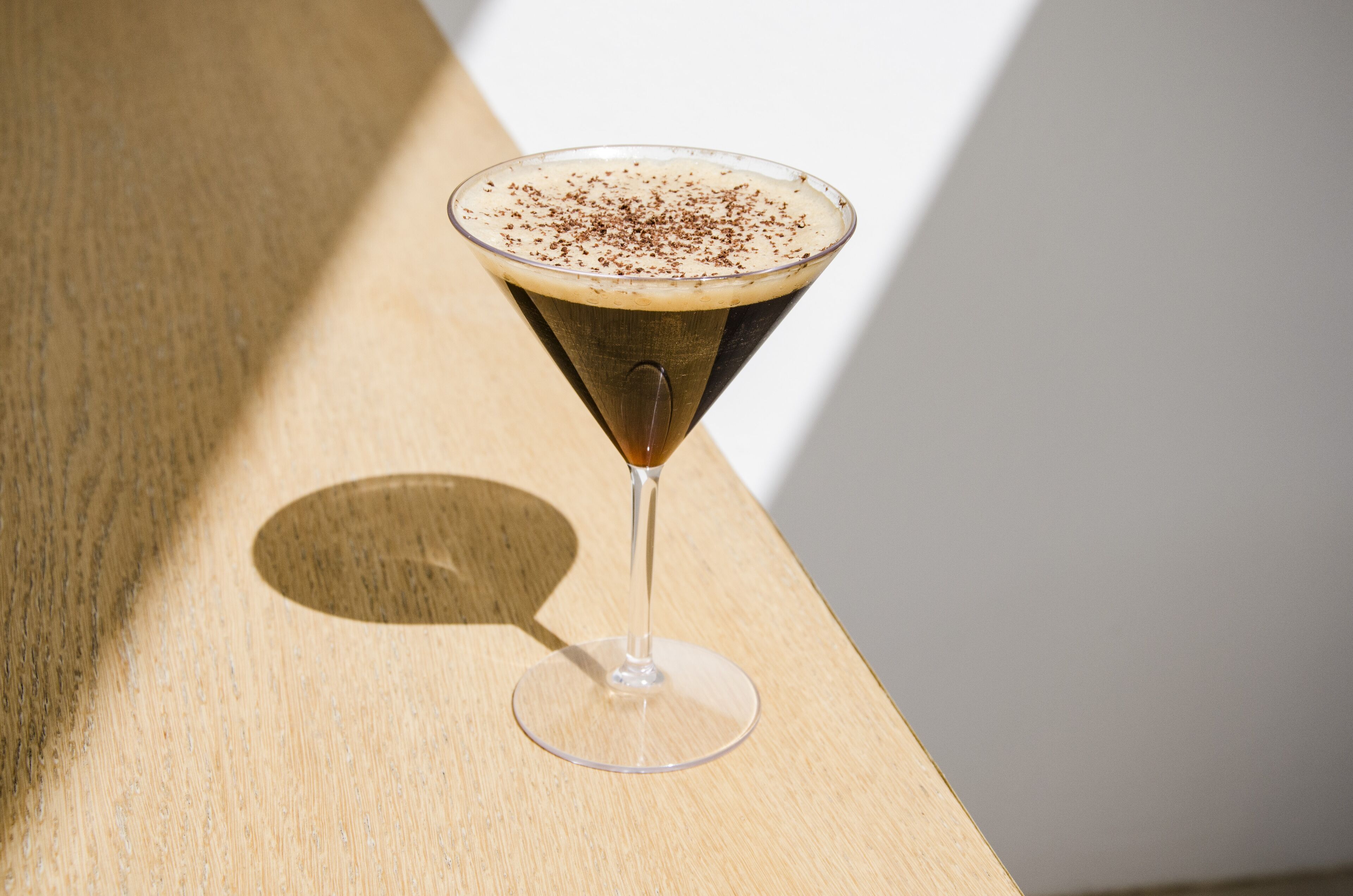 Una copa de martini con un líquido oscuro y una espuma arriba, sobre una superficie de madera.