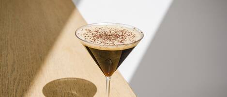 Una copa de martini con un líquido oscuro y una espuma arriba, sobre una superficie de madera.