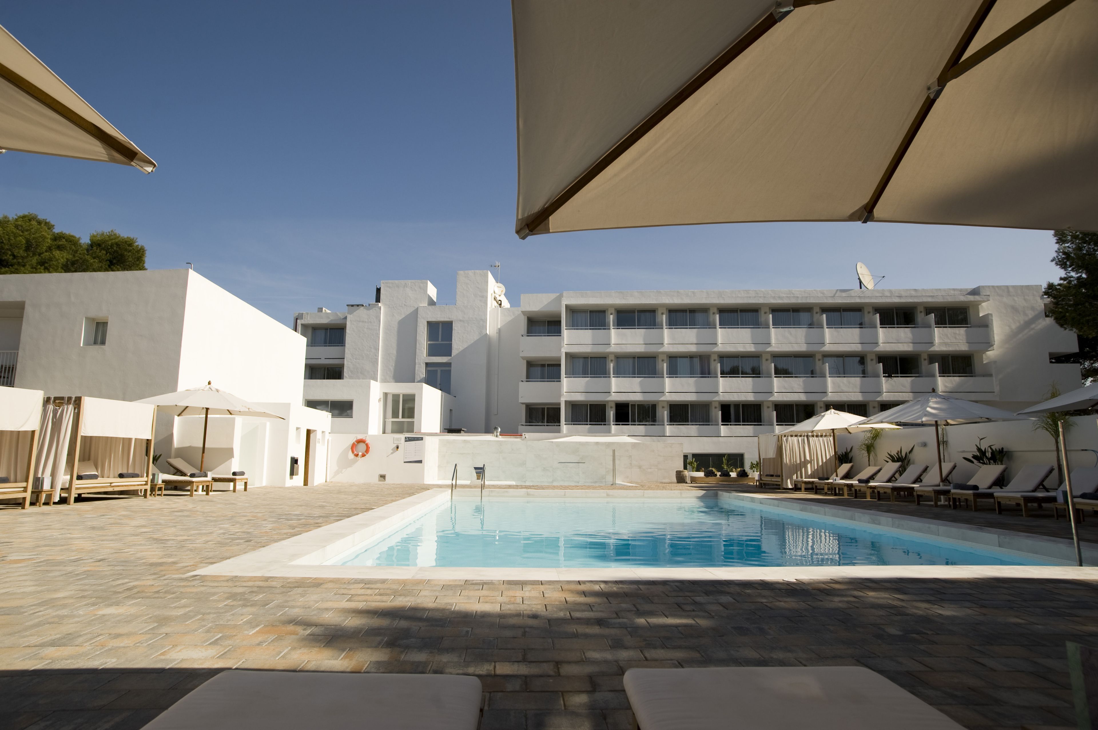 A swimming pool with lounge chairs and umbrellas, surrounded by a modern building with multiple floors and balconies.