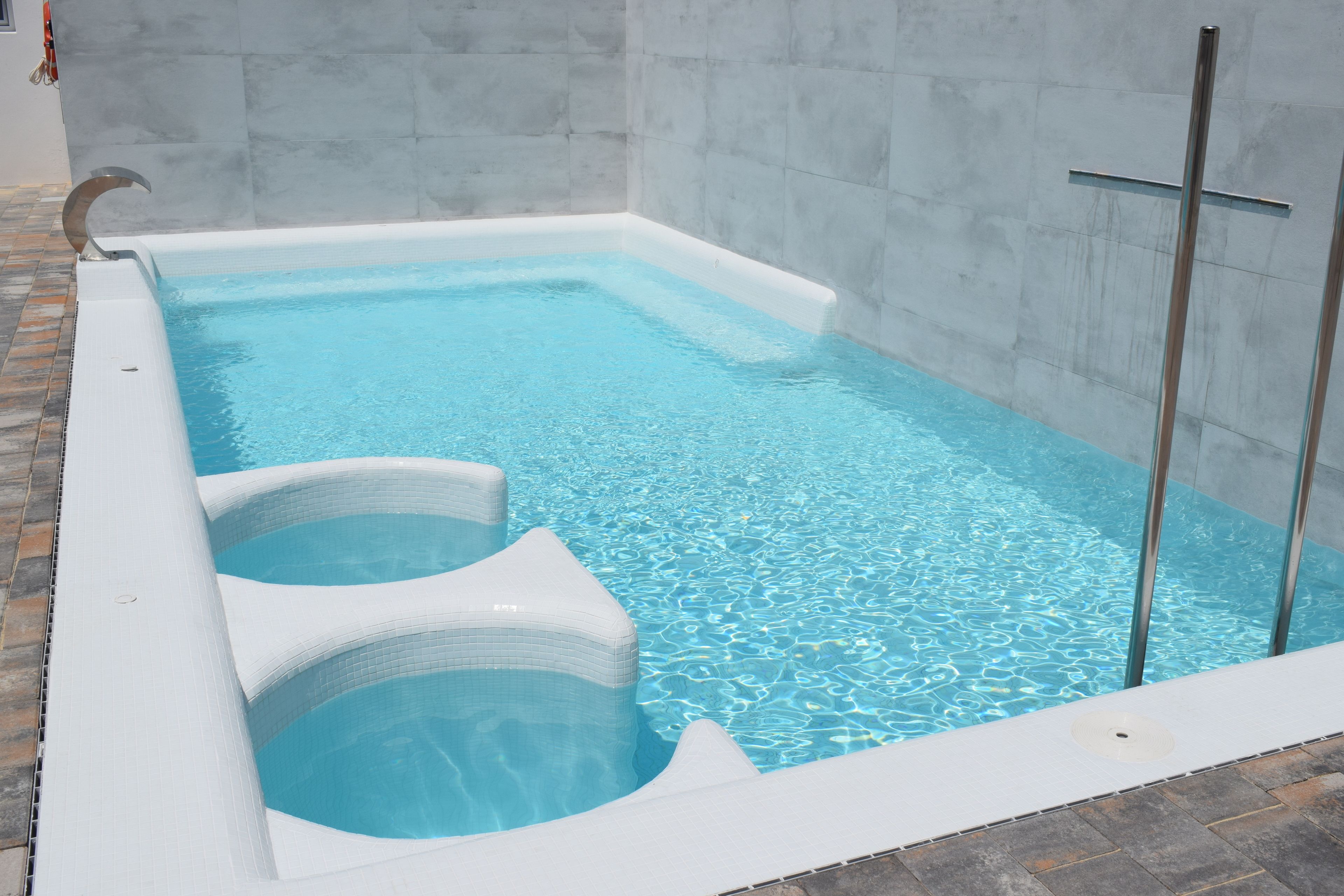 A rectangular pool with clear blue water, a white edge, and a glass partition on one side.