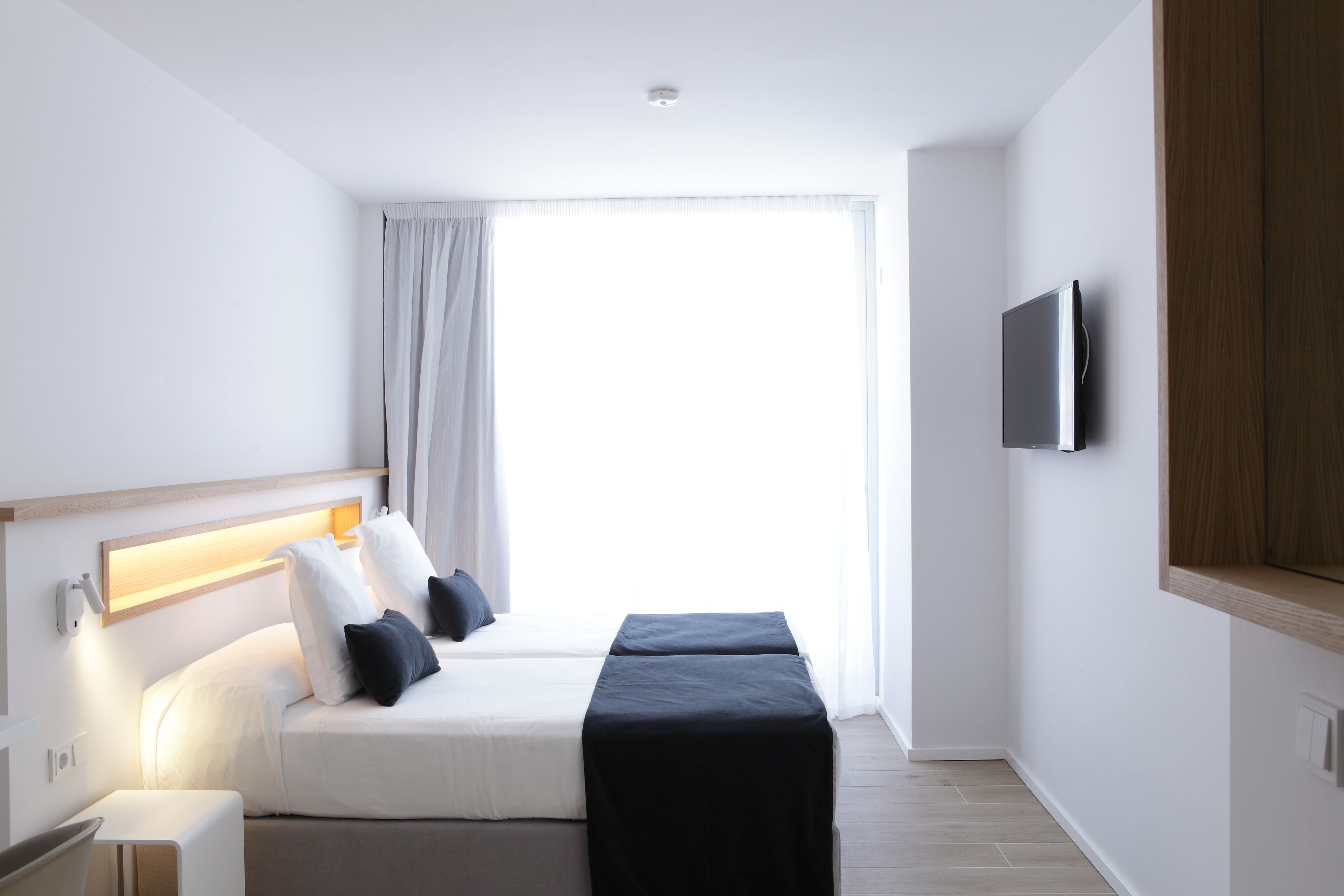Une chambre d’hôtel moderne équipée d’un lit, d’une table de chevet et d’un téléviseur fixé au mur.