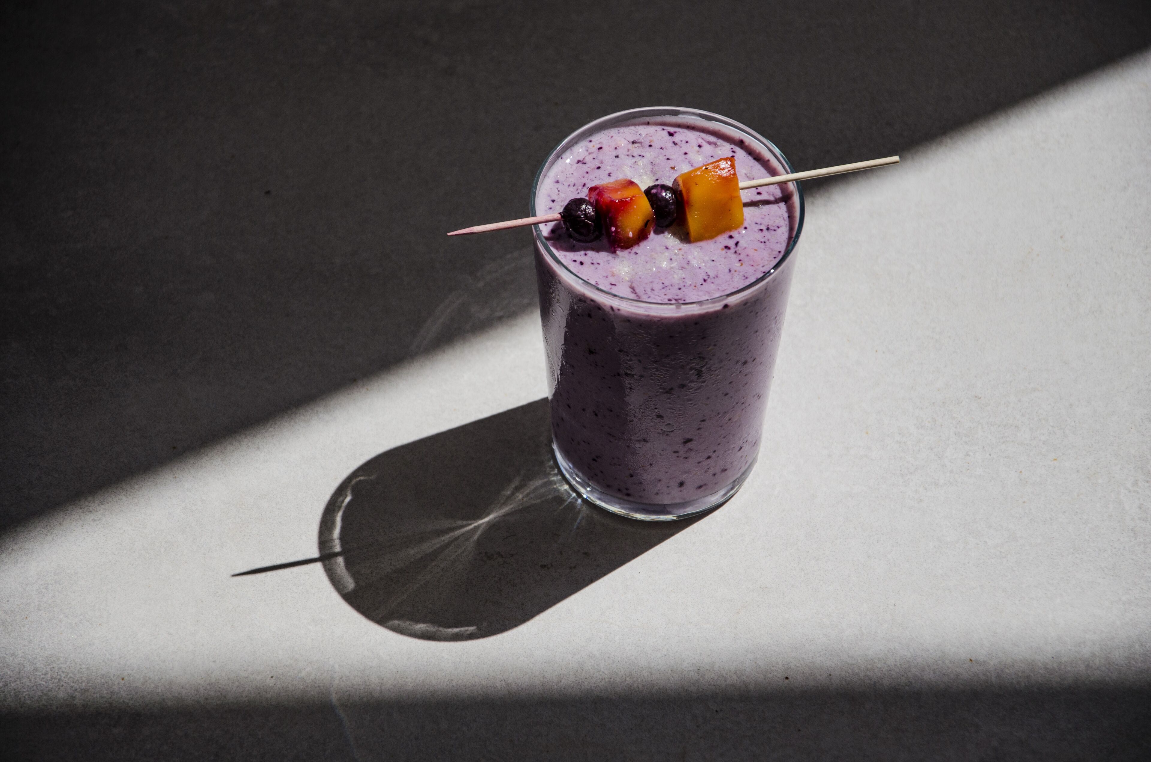 A glass of smoothie with fruit skewers on a table.