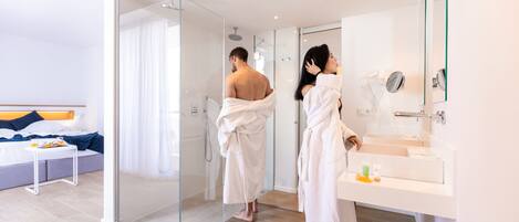 Habitación de hotel moderna con cabina de ducha de vidrio, un espejo grande y una mesita de noche con artículos de aseo.
