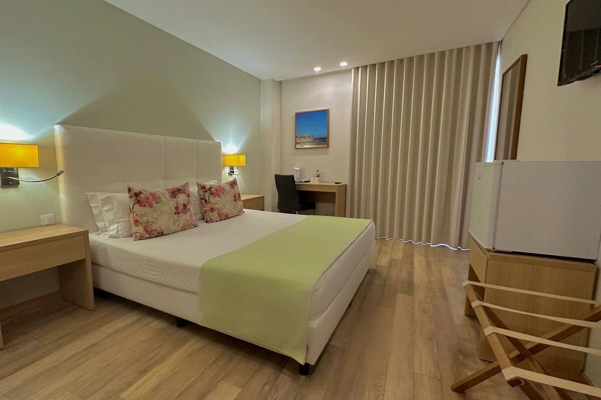 Ein Hotelzimmer mit einem Bett, Nachttischen, einem Schreibtisch, einem Sessel, einem Fernseher und einem Kleiderschrank.