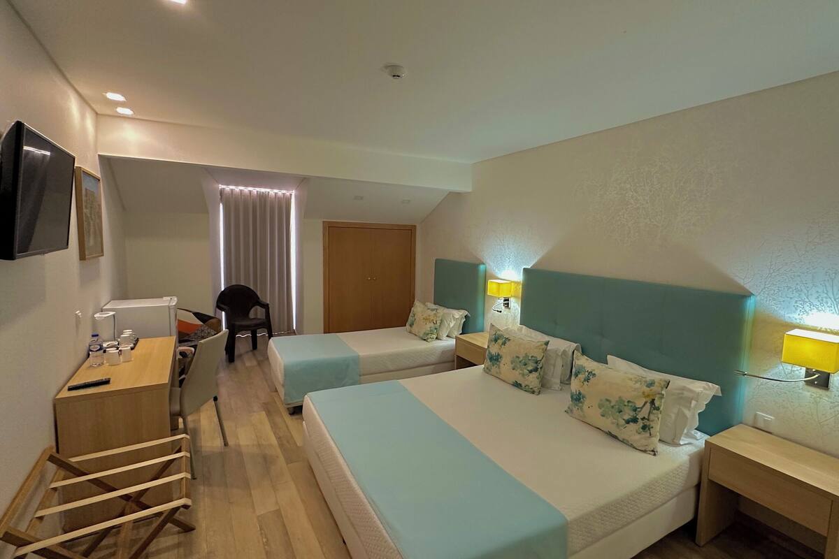 Ein Hotelzimmer mit zwei Betten, einem Schreibtisch, einem Stuhl, einem Fernseher und einem fenster mit Vorhängen.