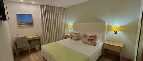 A hotel room with a bed, bedside tables, a desk, a chair, a lamp, and a painting on the wall.