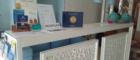 Un mostrador de recepción con un cartel que indica una calificación de 9.2, una pizarra de menú y una zona de estar acolchada en azul.