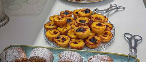 Uma mesa de buffet com diversos doces e sobremesas, incluindo tartes e pastéis, dispostos em pratos e bandejas.