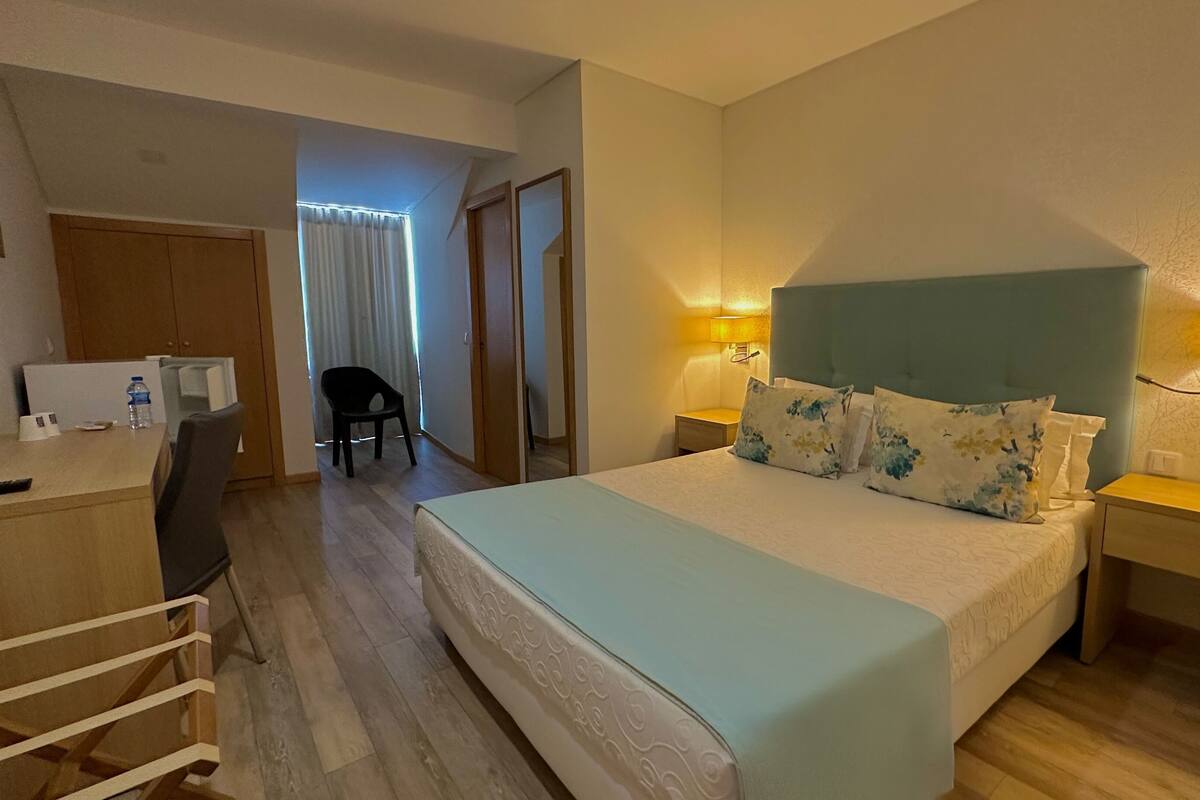 Ein Hotelzimmer mit Bett, Nachttischen, Schreibtisch, Stuhl und einer Wasserflasche.
