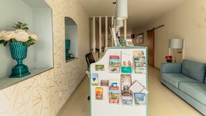 A reception area with a white reception desk, a blue sofa, a vase with flowers, and a wall with a leaf pattern. - Sea Garden Residência (Peniche)