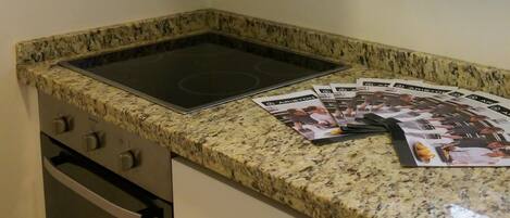 A compact kitchen with a granite countertop, stainless steel oven, and a window above the sink.
